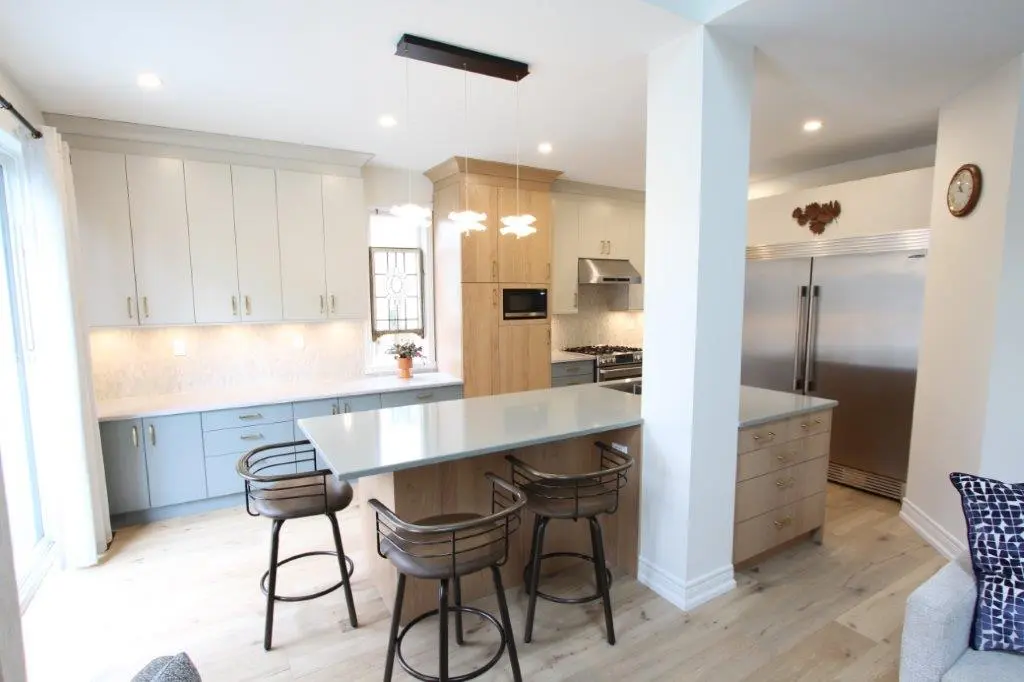 Modern kitchen with light wood flooring, a large island with bar stools, white and blue cabinets, and stainless steel appliances.