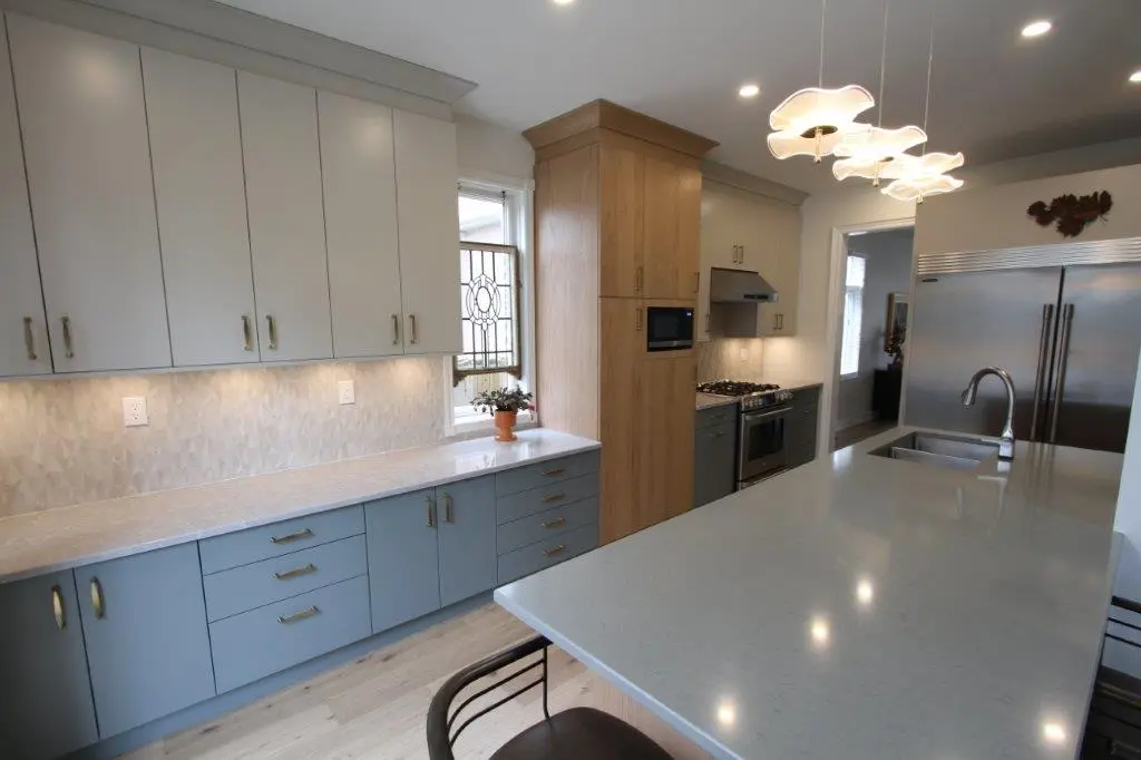 Modern kitchen with light gray cabinets, large island with sink, stainless steel appliances, and pendant lighting.