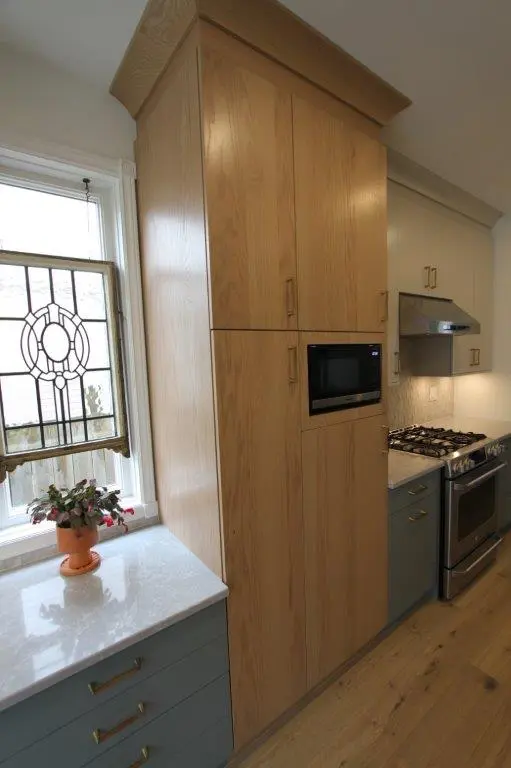 Modern kitchen with light wood cabinetry, built-in microwave, and stovetop with oven, next to a window with a decorative stained glass design.