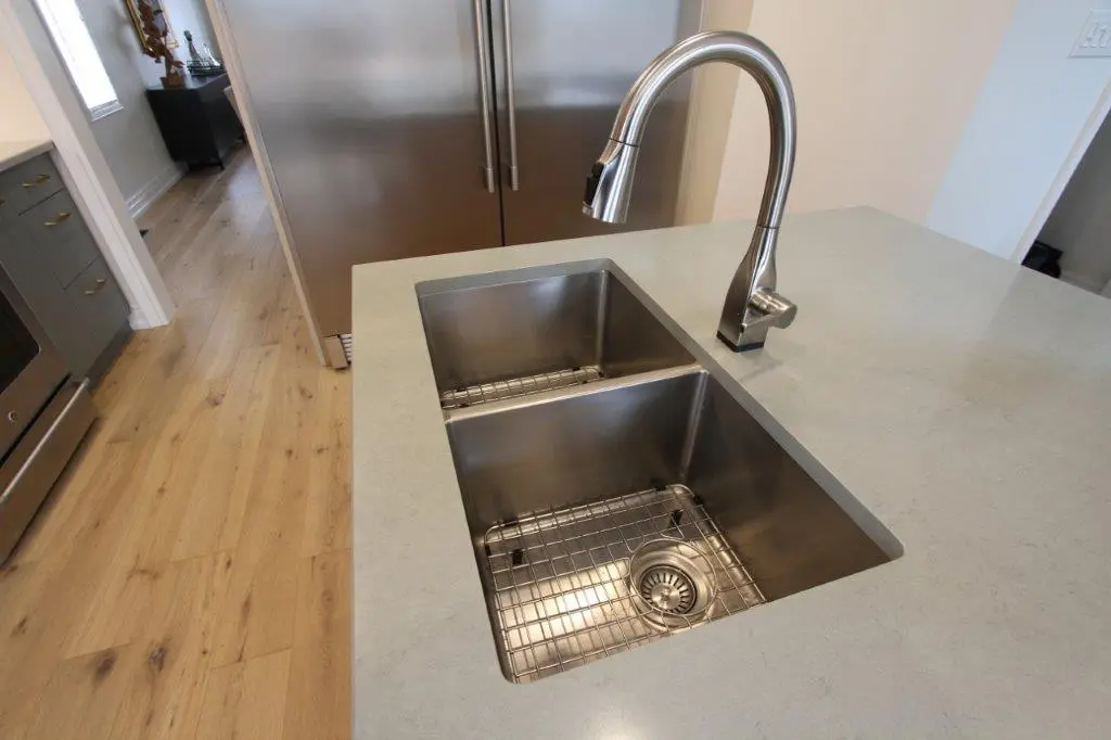 A modern kitchen sink with a dual-basin stainless steel design and a chrome faucet, installed in a light-colored quartz countertop.