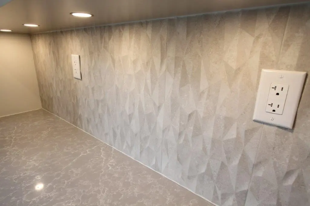 A kitchen backsplash with a textured geometric pattern and under-cabinet lighting illuminating the area. The quartz countertop has a marbled design.