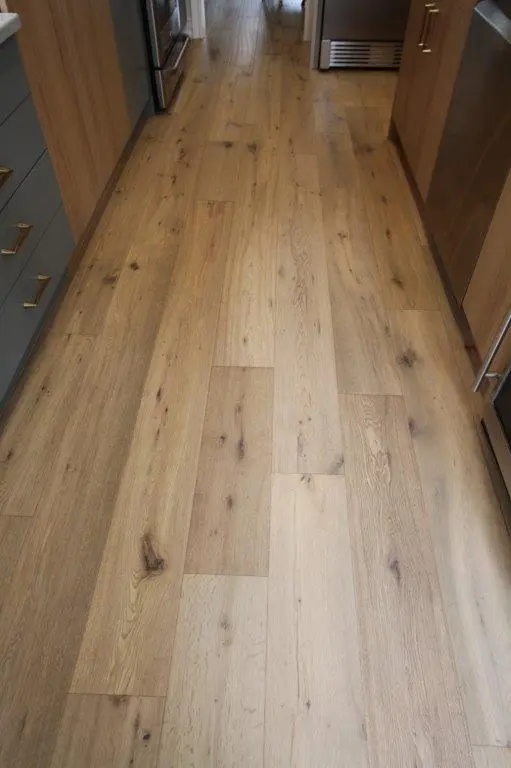A kitchen with light-colored wooden flooring and cabinets, featuring a stainless steel oven and other appliances along the sides.