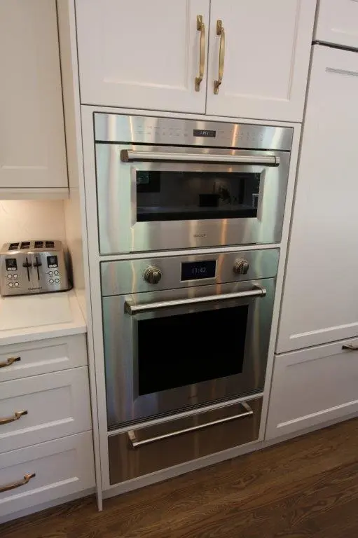 A modern kitchen with stainless steel wall oven and microwave installed in white cabinetry, adjacent to a countertop with a four-slice toaster.