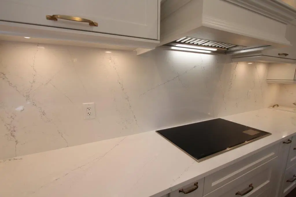 Modern kitchen with white quartz countertops and backsplash, featuring a sleek black stovetop and under-cabinet lighting.