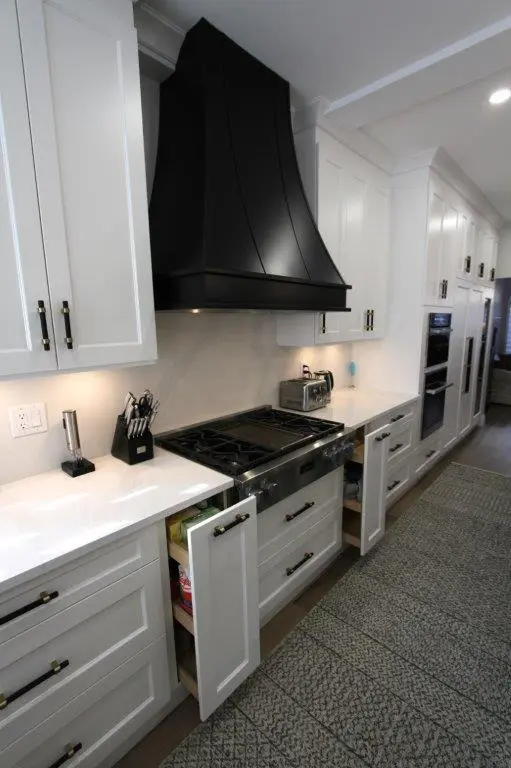 Modern kitchen featuring white cabinetry, a black range hood, a stainless steel stove, and a countertop with a knife block and small toaster oven; some cabinet doors are slightly open, revealing shelving inside.