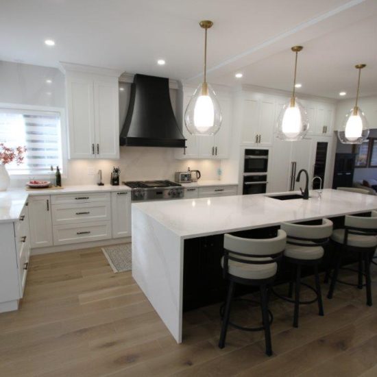Modern kitchen with white cabinets, a large black range hood, a central island with white countertop and bar stools, and pendant lights overhead.