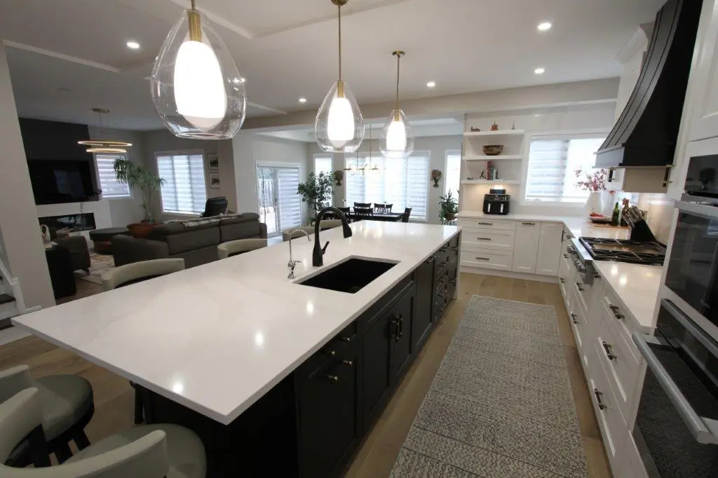 Modern kitchen with a large white quartz island countertop, black sink, pendant lights, white cabinets, and stainless steel appliances.