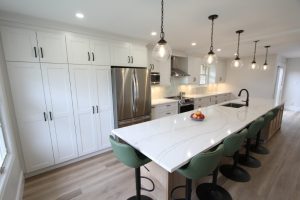 Modern kitchen with a large quartz island, green bar stools, stainless steel appliances, and pendant lighting.