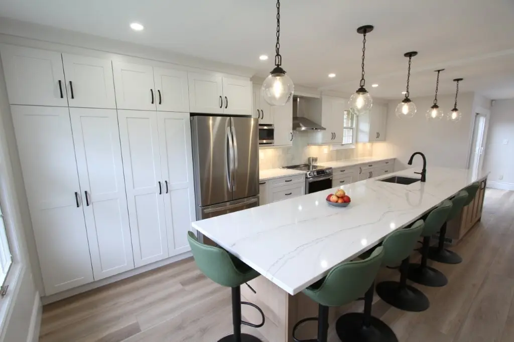 Modern kitchen with a large quartz island, green bar stools, stainless steel appliances, and pendant lighting.