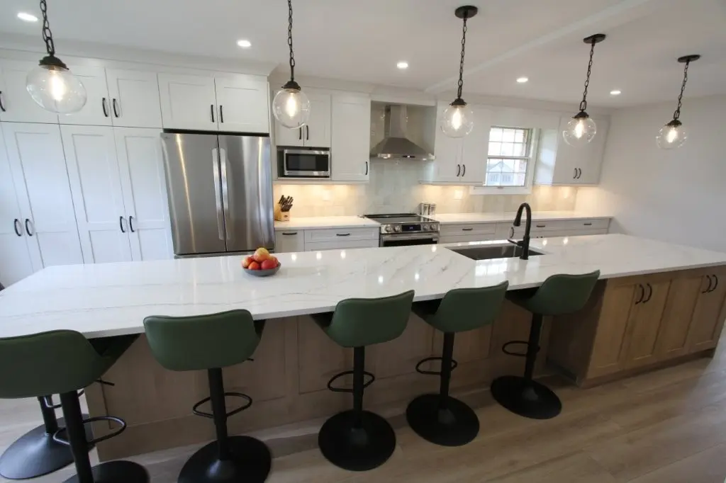 Modern kitchen with a large white quartz island, green bar stools, stainless steel appliances, and hanging pendant lights.