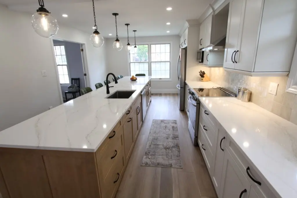 Modern kitchen with white countertops, wooden cabinets, black sink fixtures, pendant lighting, and stainless steel appliances.