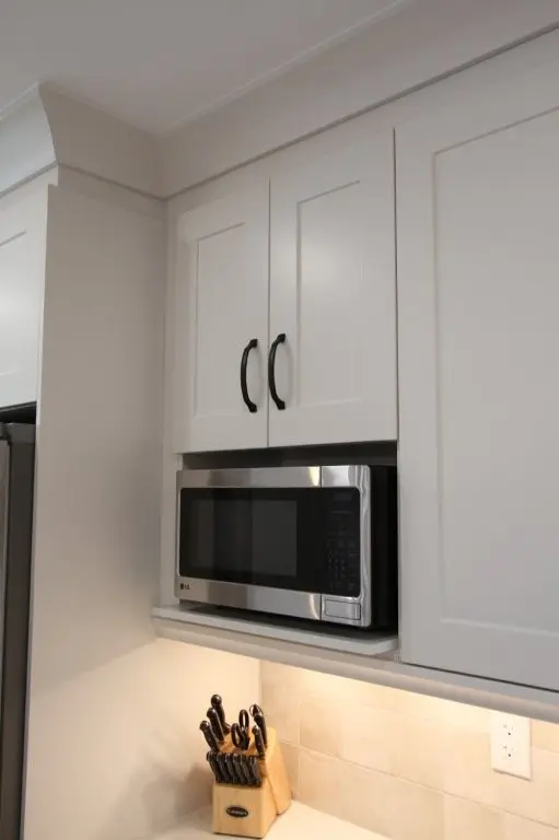 A modern kitchen with white cabinets featuring a built-in microwave and a block of knives on the countertop.