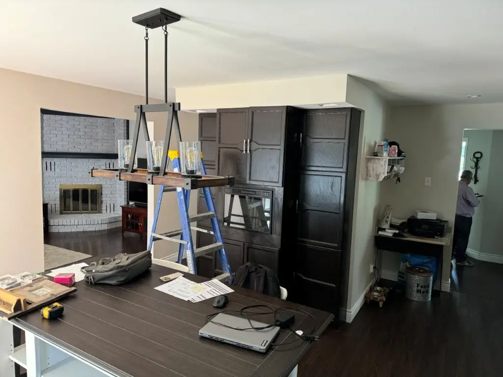 A before renovation scene with dark wood cabinets, a fireplace with a white brick surround, and a ceiling light fixture.