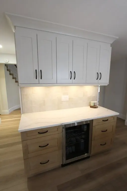 A modern kitchen with light-colored upper and lower cabinets, a backsplash with square tiles, and a quartz countertop featuring a built-in wine cooler.