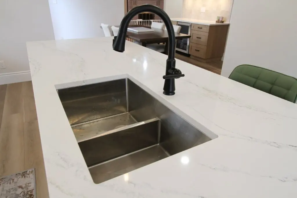 A modern kitchen with a white quartz countertop featuring a rectangular stainless steel sink and a black faucet.
