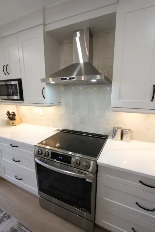 Modern kitchen with a sleek stainless steel stove and range hood, surrounded by white cabinetry and a quartz countertop; a microwave is integrated into the cabinets, and a knife block is placed on the countertop.