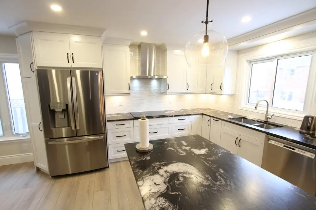 Bright modern kitchen with white cabinetry, stainless steel appliances including a French door refrigerator and dishwasher, black and white marbled countertops, and a large window above the sink.