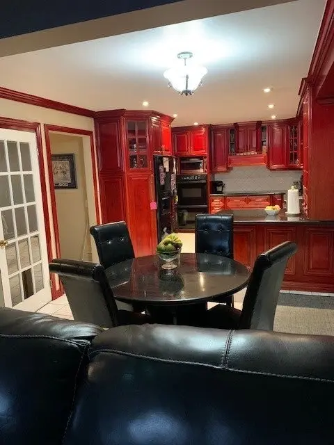 A before picture of a Kitchen with dark wooden cabinets, black appliances, and a round black dining table with four black cushioned chairs, viewed from behind a black leather couch