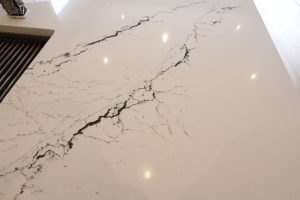 Close-up of a white quartz countertop with black veining and reflections of ceiling lights, alongside a portion of a kitchen sink area.