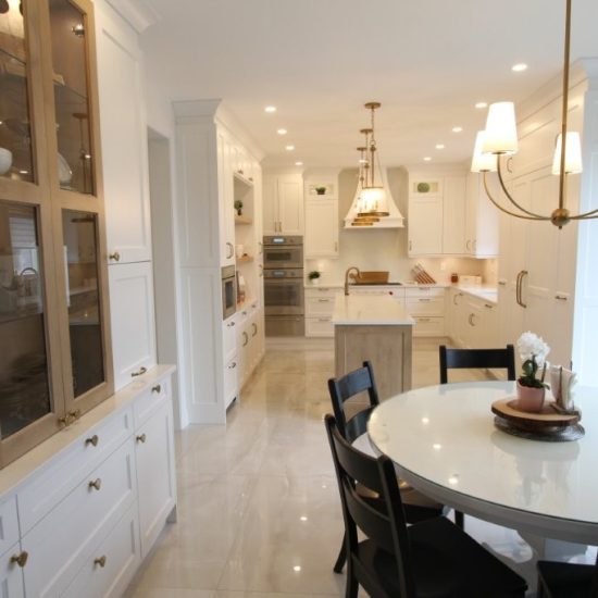 Bright modern kitchen with white cabinetry, a central island with a sink, pendant lighting, and a round dining table surrounded by black chairs, featuring a small plant centerpiece.