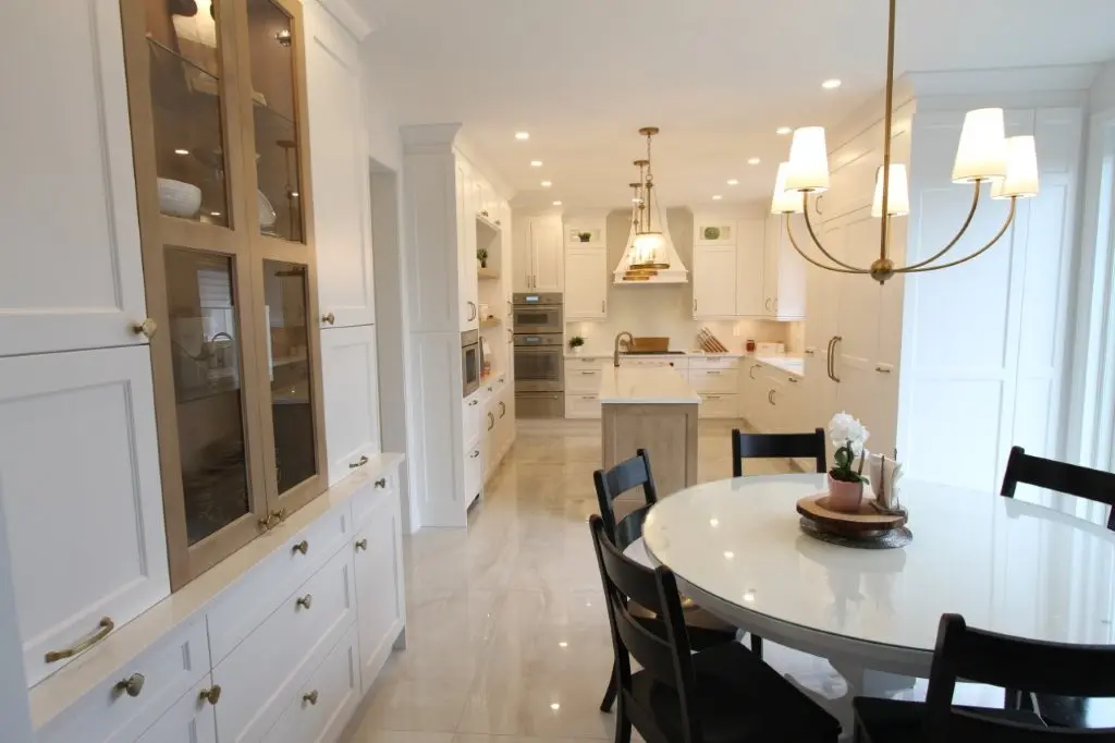 Bright modern kitchen with white cabinetry, a central island with a sink, pendant lighting, and a round dining table surrounded by black chairs, featuring a small plant centerpiece.