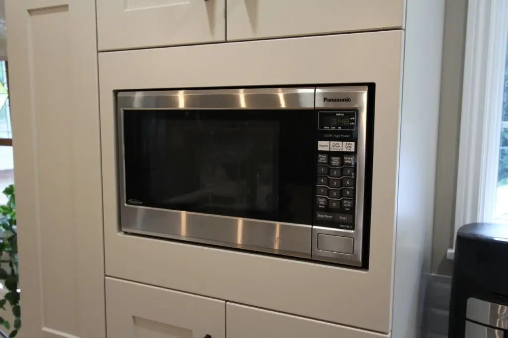 Built-in stainless steel Panasonic microwave oven installed in a white kitchen cabinet with a digital display and control panel on the right side.