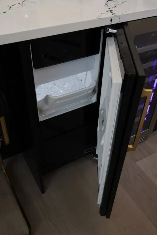 Open black compact freezer drawer under a marble countertop filled with ice cubes, viewed from the side in a modern kitchen setting.