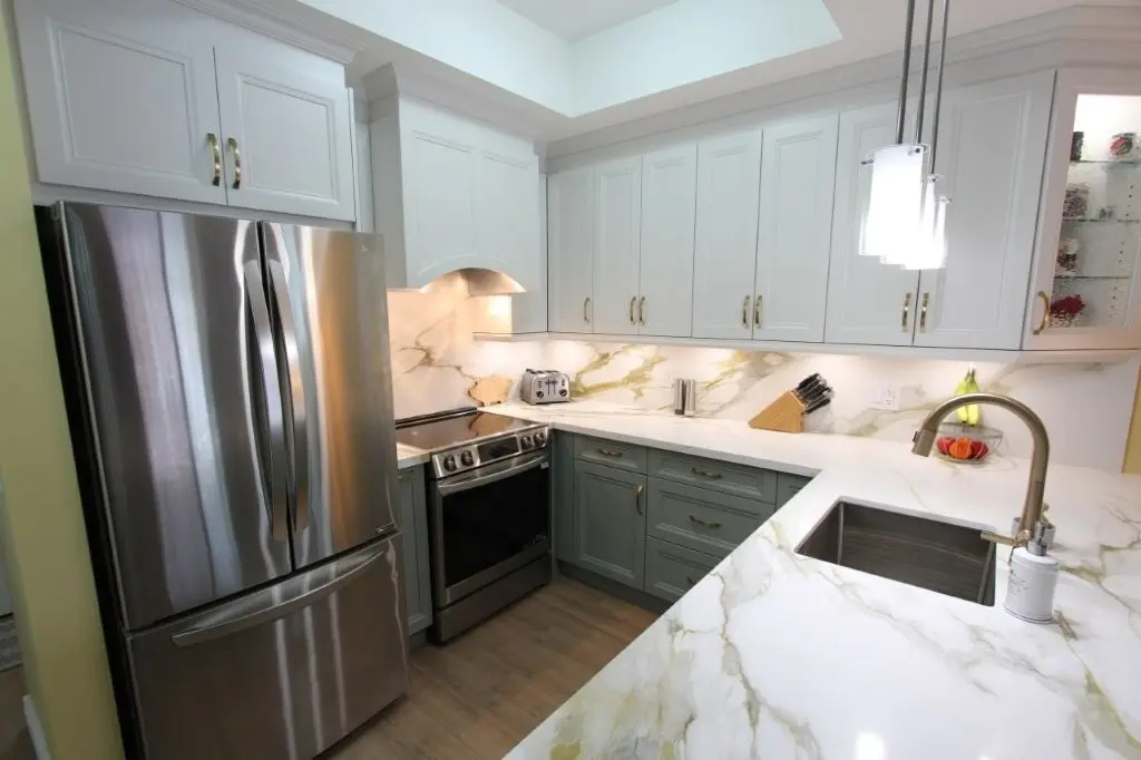 Modern kitchen interior with two-tone cabinetry, stainless steel refrigerator and stove, quartz countertops and backsplash, under-cabinet lighting, and a sink with a high-arc faucet under pendant lights.