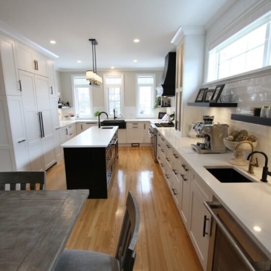 Bright modern kitchen with white cabinets, central island, wood floors, long countertop with sink and coffee maker under windows