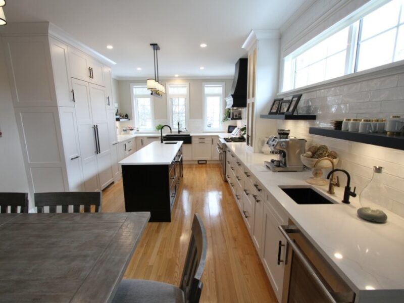 Bright modern kitchen with white cabinets, central island, wood floors, long countertop with sink and coffee maker under windows