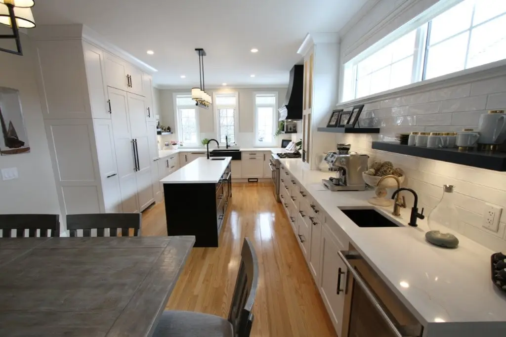 Bright modern kitchen with white cabinets, central island, wood floors, long countertop with sink and coffee maker under windows
