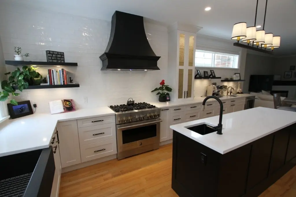Modern white kitchen with black island and hood, stainless steel gas range, pendant lights, and open shelving with plants and books