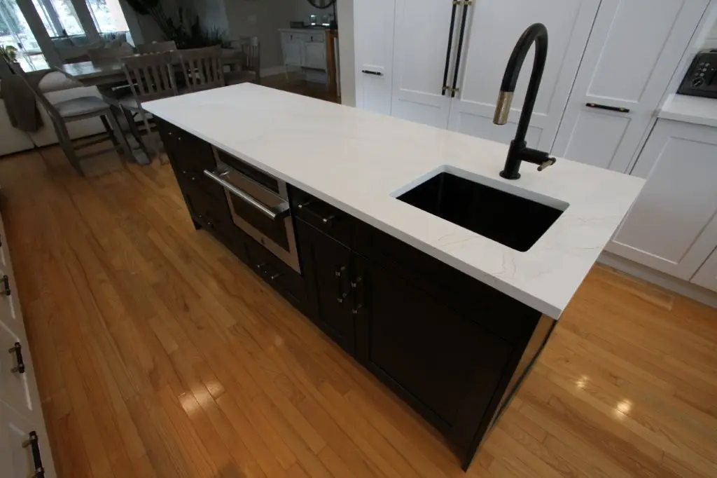 Kitchen island with white quartz countertop, black undermount sink and matte black faucet, dark cabinetry and hardwood floor