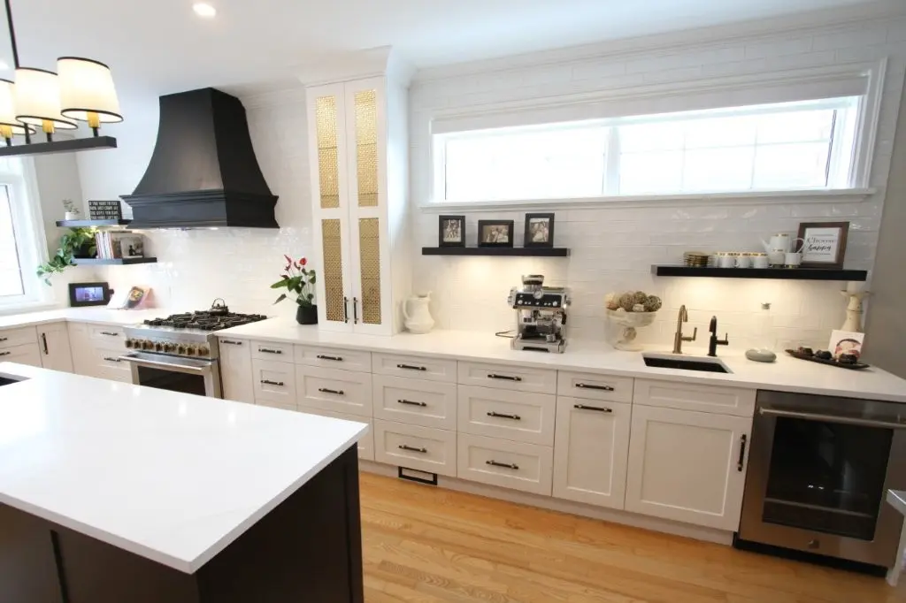 Bright modern kitchen with white cabinetry, large island, black range hood, espresso machine, and wood floors.