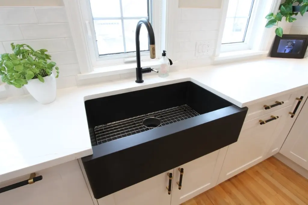 Matte black farmhouse kitchen sink with wire rack set into white quartz countertop, black and gold pull down faucet