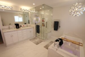 Spacious modern white bathroom with double-sink vanity, glass-enclosed shower, built in tub with wooden tray, and decorative lighting