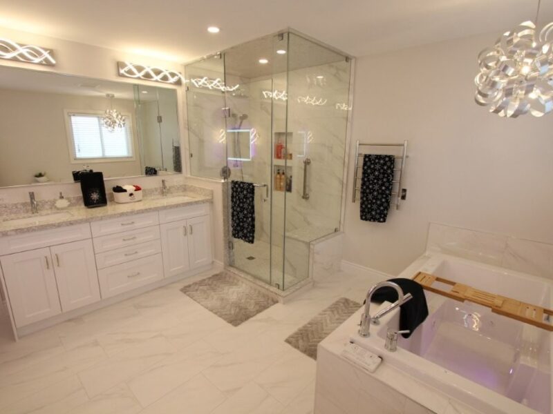 Spacious modern white bathroom with double-sink vanity, glass-enclosed shower, built in tub with wooden tray, and decorative lighting