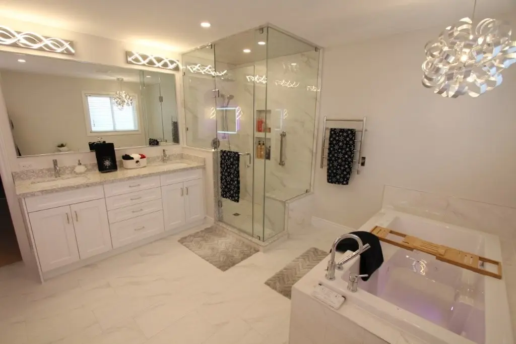 Spacious modern white bathroom with double-sink vanity, glass-enclosed shower, built in tub with wooden tray, and decorative lighting