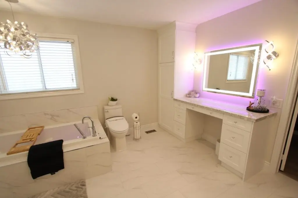 Bright modern bathroom with white porcelain floor, built-in bathtub, toilet, and illuminated makeup mirror with purple backlighting.