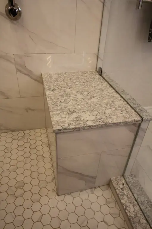 Corner shower bench with speckled Quartz top and porcelain 'marble-effect' tiled sides and hexagonal floor tiles inside glass enclosure
