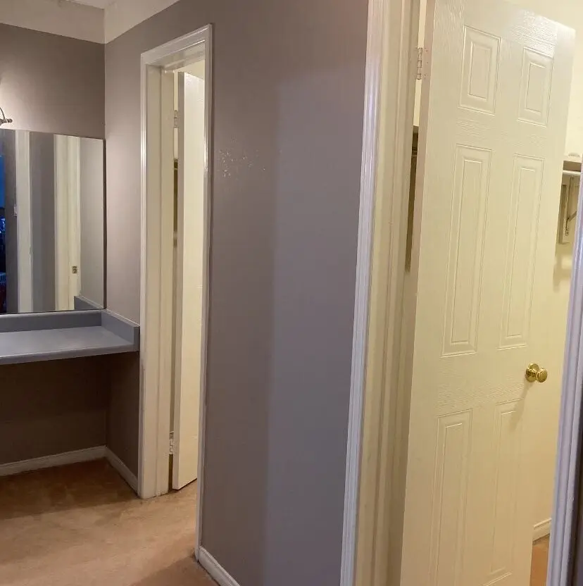 Before picture of hallway with a small built-in makeup desk and mirror on the left, and open white doors to the double closets on the right.