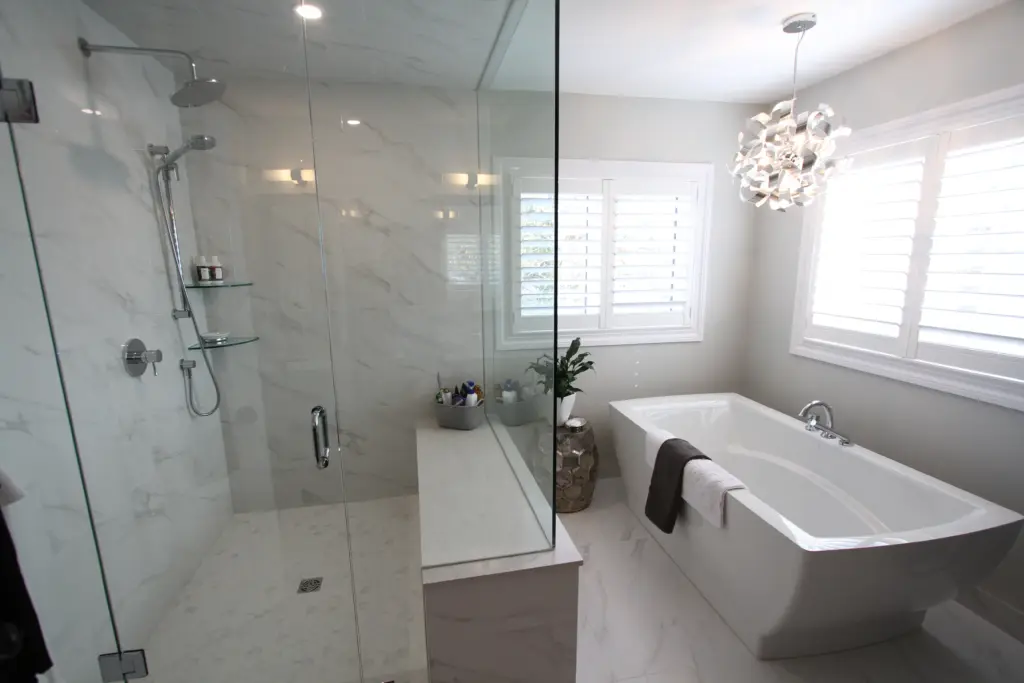 Modern bathroom with glass-enclosed marble shower, freestanding tub, white shutters and decorative pendant light