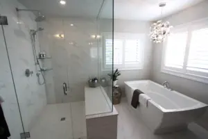 Modern bathroom with glass-enclosed marble shower, freestanding tub, white shutters and decorative pendant light