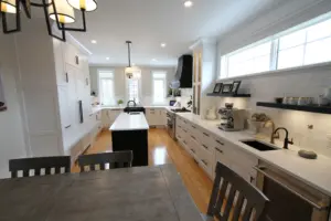 Bright modern kitchen with white cabinets, central island, wood floors, long countertop with sink and coffee maker under windows