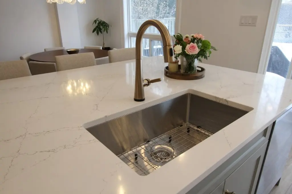 Modern kitchen island with white countertop, stainless sink, brass faucet, and flowers in the background