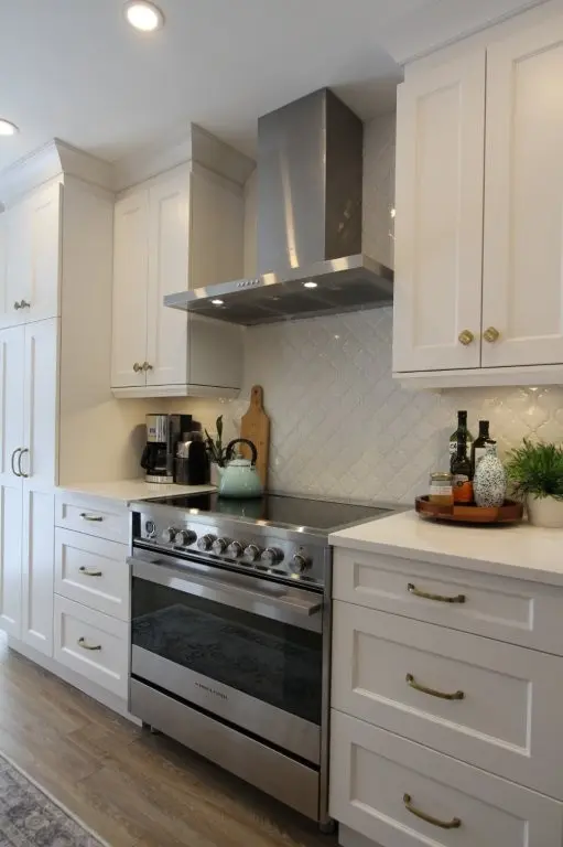 Bright white kitchen with a stainless steel range, hood, and cabinets, plus a countertop coffee setup and decor