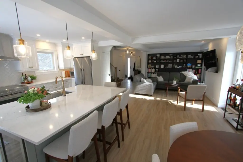 Bright open-concept kitchen and living room with a large island, pendant lights, and gray sectional sofa
