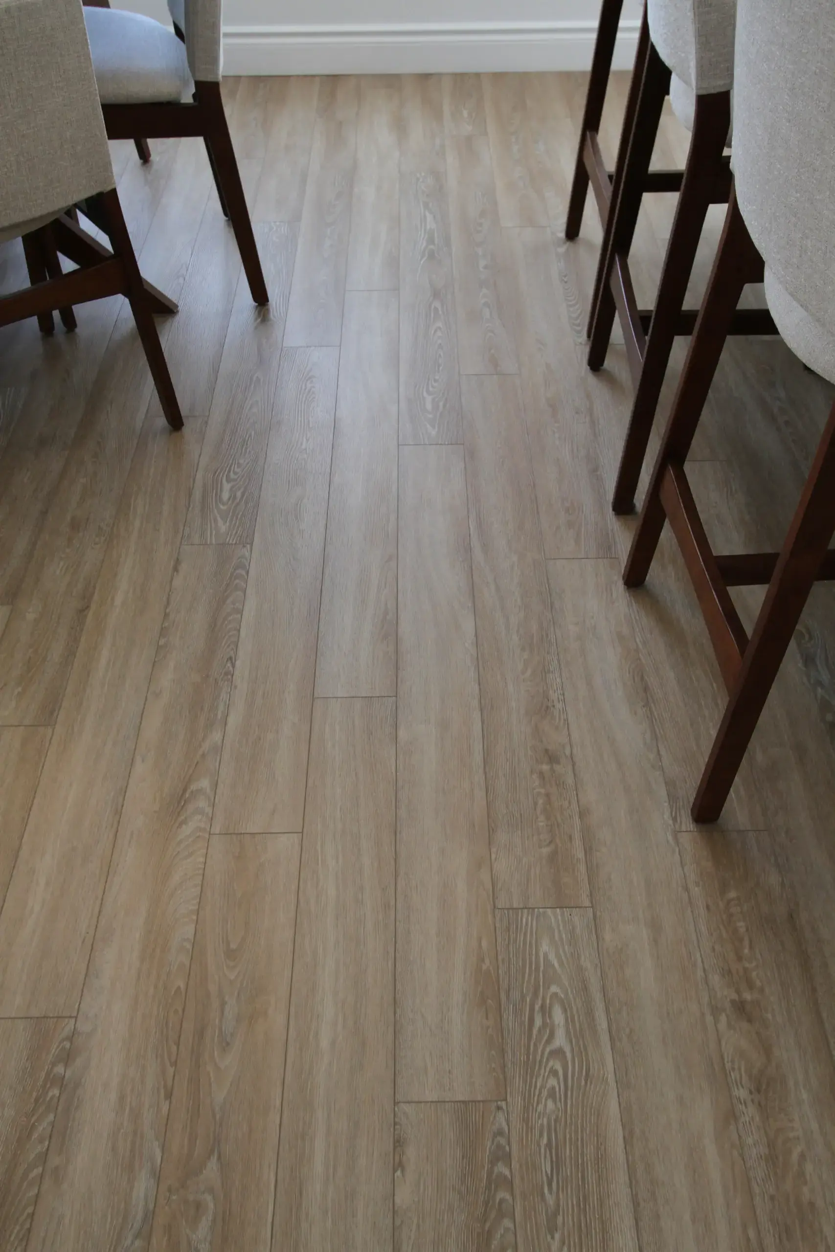 Light wood plank floor beside dark wooden chair legs and beige upholstered seats in a dining area