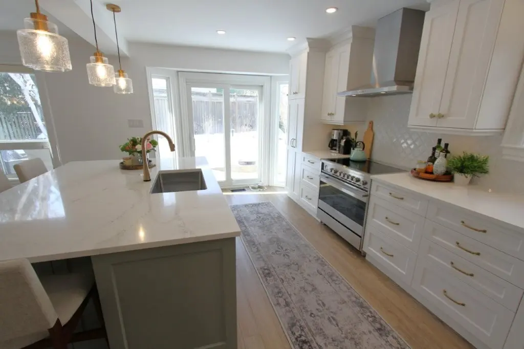 Bright modern kitchen with white cabinets, marble island, pendant lights, and sliding glass doors to a backyard