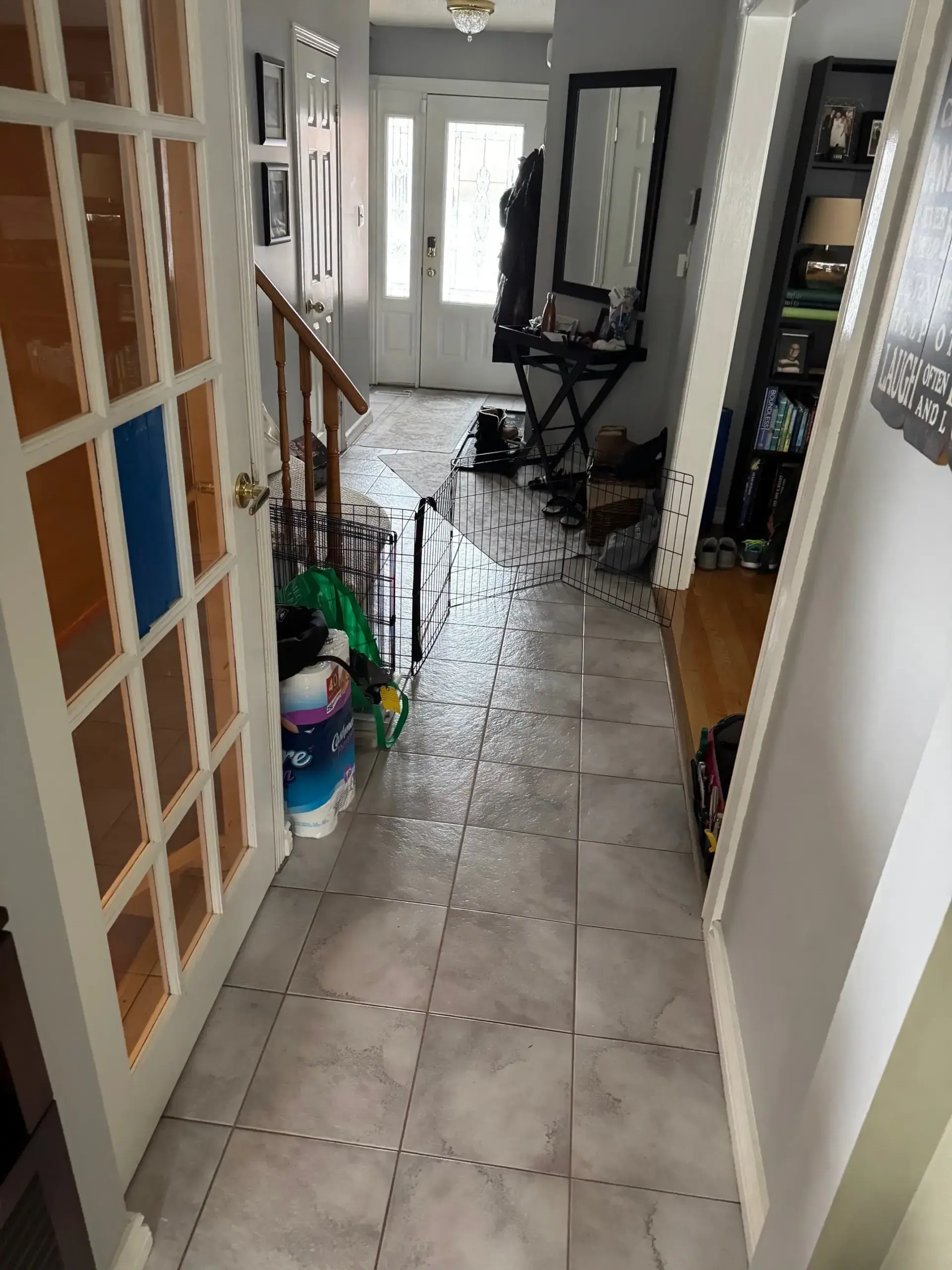 Hallway with tiled floor, a glass-paneled door, mirror, shelving, and pet gates blocking the passage